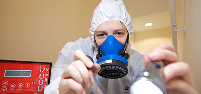 Asbestos analyst completing a visual inspection using a torch. Red air testing pump in the background.